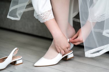 Bir gelin beyaz topuklarını nazikçe bağlar, düğününden önce sessiz bir hazırlık anı. Ayakkabılar zarif ve şık, günün beklentisini yansıtıyor..