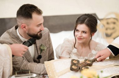 Bir düğün töreninde çekilen hassas bir an. Gelin ve damat törene katılırken birbirlerine sevgi dolu bakışlar atıyorlar. Önlerinde dini bir haç var..