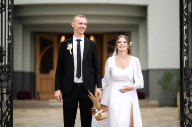 Bir gelin ve damat, zarif giyimli, düğünlerinden sonra binadan çıkıyorlar. Küçük bir çiçek sepeti tutuyorlar, neşe ve mutluluk saçıyorlar..