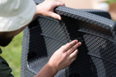 Koyu renkli dokuma mobilyaları birleştiren ellerin yakın çekimi. Malzeme reçine hasırına benziyor. İki parçanın bağlantısına odaklan..