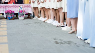 Basit beyaz elbiseler ve beyaz ayakkabılar giyen bir dizi kadın sabırlı bir şekilde ayağa kalkın. Arkalarındaki masada iki sepet var..