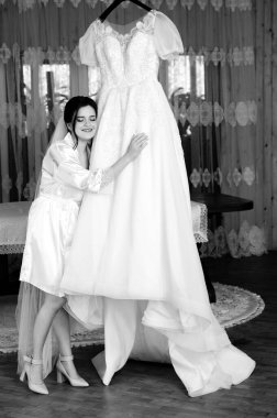 İpek bornozlu bir gelin baş döndürücü gelinliğini nazikçe kucaklıyor. Sahne, yaklaşan düğün töreni için duygu ve heyecanla dolu..