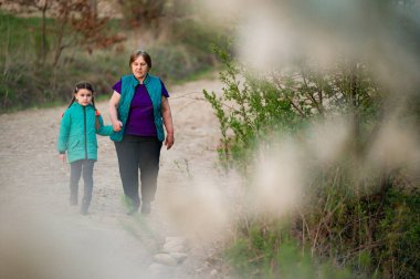 Yaşlı bir kadınla genç bir kızın toprak bir yolda el ele yürüdükleri yürek ısıtan bir sahne. Odak yumuşak, sakin bir atmosfer yaratıyor. Yol doğal bir ortamda esiyor..