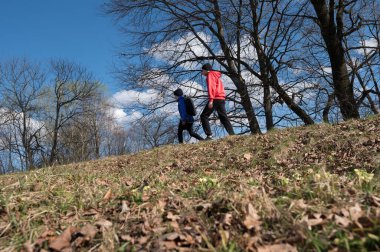 Bir çift çimenli bir tepe boyunca yürüyor, yukarıdaki mavi gökyüzünü çevreleyen ağaçlar. Yol dökülen yapraklarla dolu, bu da sonbahar ya da ilkbahar başlarını işaret ediyor..