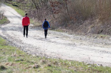 İki genç çocuk sessiz bir çakıl yolunda yürüyor. Çevredeki bitki örtüsü kıt, bu da baharın geldiğini gösteriyor. Huzurlu ve huzurlu bir sahne..
