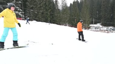 İki snowboardcu, karla kaplı bir dağ ortamında yumuşak bir yamaçtan aşağı süzülüyorlar. Kışın eğlenen bireyler üzerinde yoğunlaşıyoruz..