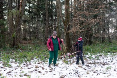 Bir yetişkin ve küçük bir çocuk kırsal bir kızak taşıyarak karlı bir orman yolunda ilerliyorlar. Sahne huzurlu ve bir kış macerası hissi uyandırıyor..
