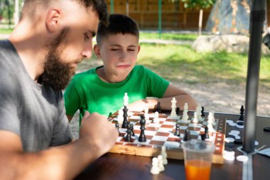 Sakallı bir adam ve genç bir çocuk açık havada satranç oyununa çok dalmışlar. Güneş ışığı satranç tahtasını aydınlatır ve sonraki hamlelerini belirler..