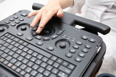 Ultrason makinesi kullanan bir tıp uzmanının yakından görüntüsü. Görüntü, kontrol panelinde gelişmiş teşhis ekipmanlarını vurgulayan bir eli gösteriyor..