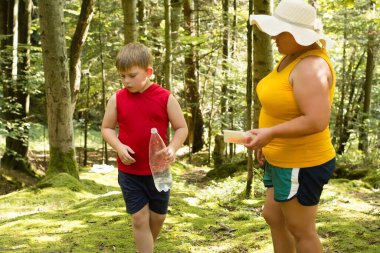 Genç bir çocuk ve yetişkin bir kadın orman yolunda yürüyor. Çocuk bir su şişesi taşıyor, kadın da bir kap tutuyor. Doğanın sükuneti onları sarar..