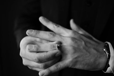 Bir adamın yüzüğünü dikkatlice tutarken çekilmiş siyah beyaz bir görüntüsü. Sahne, samimiyet ve tefekkür duygularını çağrıştırıyor..