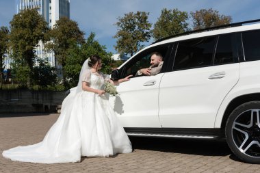 Göz kamaştırıcı beyaz elbiseli bir gelin, parlak beyaz bir SUV içinde oturan damadı ile etkileşime girer. Sahne neşeli, evlilik hayatlarının başlangıcı..