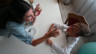 Sıcak bir mutfakta, neşeli bir anne oğlunu doyurur, ortak yemeklerine mutluluk getirir. Lezzetli yemeklere kahkahalarla gülüyorlar..