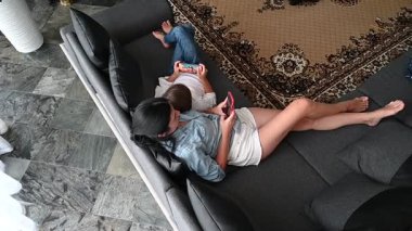 Oksana Eney çocuğu yakınlarda oyun oynarken rahat bir şekilde kanepede uzanıyor. Konforlu oturma odasında şık bir dekor ve güzel bir halı var. Sıcak bir atmosfer yaratıyor..