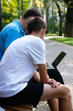 İki genç erkek öğrenci, açık hava ortamının ortasında parktaki bankta otururken bir dizüstü bilgisayarla iş birliği yapıyorlar. Bu sahnede akademisyenlere odaklı gelişigüzel bir öğrenme ortamı tasvir ediliyor.