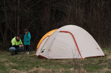 Bir baba ve kızı, uzun otlar ve ağaçlarla çevrili kamp çadırlarının yakınında eğlenceli bir aktiviteye girişiyor, sakin bir manzarada birlikte güzel vakit geçiriyorlar..