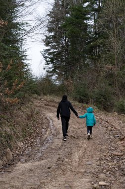 Uzun ağaçlarla çevrili engebeli toprak bir patika boyunca el ele yürüyen iki figür, sakin bir günde doğanın güzelliğini ve dostluğunu gözler önüne seriyor..