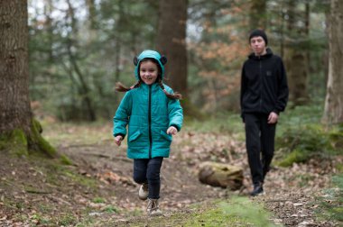 Deniz mavisi ceketli genç bir kız sevinçle önde koşarken genç bir oğlan onun arkasında sakince geziniyor. Huzurlu orman sonbahar renklerini ve benekli güneş ışığını sergiliyor..