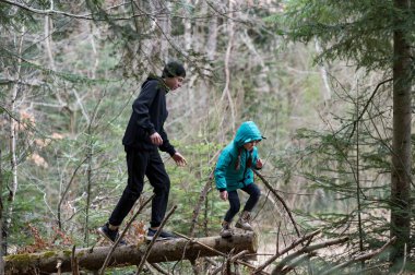 İki çocuk sık bir ormanda neşeli bir şekilde geziniyor. Etrafı canlı yeşilliklerle ve serin bir günün yumuşak sisinin altında yükselen ağaçlarla çevrili..