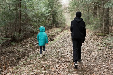 İki çocuk, uzun ağaçlar ve düşen yapraklarla çevrili bir orman yolunda serin ve sakin bir günde vahşi doğanın huzurunun tadını çıkarıyorlar..