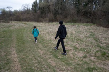 İki çocuk doğal bir ortamda çimenli bir yolda geziniyor, ağaçların arasında sessizce geziniyor ve baharın erken saatlerinde hafif bir meltem esiyor..