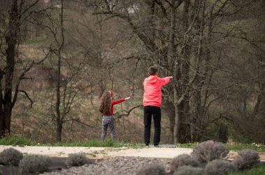 İki çocuk, sakin bir günde çıplak ağaçlar ve mis kokulu lavanta bitkileriyle çevrili, huzurlu bir açık hava ortamında mutlulukla mesafeyi işaret ediyor..