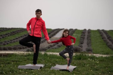 İki kardeş, dingin lavanta tarlasında yoga minderleri üzerinde neşeli bir poz veriyorlar, sakin bir öğleden sonra sevgi dolu bir anın tadını çıkarırken etrafları canlı çiçeklerle çevrili..