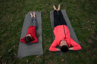 Canlı yeşil bir parkta yoga minderlerinde uzanan iki çocuk güneşli bir günün tadını çıkarıyorlar. Parlak ceketli çocuk ve rahat giyimli kız kahkahalar atıyor, dışarıda neşeli anılar yaratıyor..