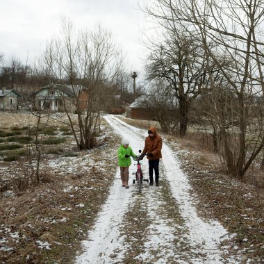 Sıcak giyimli çocuk huzurlu bir kış gününde bir bakıcının yanında bisiklet sürmeyi öğrenir. Doğa ve kırsal evler etraflarını sararken kar yolun tozunu alır..