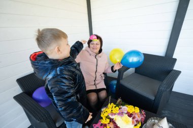 Bir çocuk, elinde canlı balonlar ve gülücükler tutarken mutluluğunu gösteren bir kadınla şakacı bir şekilde etkileşime girer. Samimi ortam onların neşeli bağlantılarını güçlendiriyor..