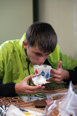 Genç bir birey dikkatle renkli bir bardaktan su içmeye odaklanır, diğer taraftan lezzetli bir ziyafeti dengeler, huzurlu bir zevk anı yaratır..