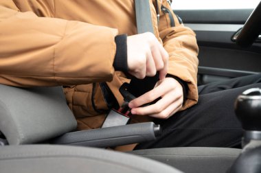 Rahat, kahverengi bir dış giysi içinde sürücü emniyet kemerini bağlar, şehir sokaklarında soğuk hava yolculuğuna hazırlanır, yolculuğa başlamadan önce güvenlik ve ihtiyatı vurgular.