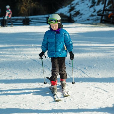 Genç bir kayakçı, renkli bir kışlık ceket ve kask giyip, aile dostu bir kayak merkezinin yamaçlarında eğlenceli bir günün tadını çıkararak, ışıl ışıl karların üzerinde rahatça dolaşır.