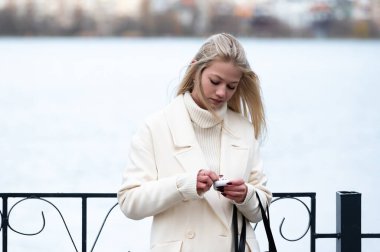Gölün kıyısında duran beyaz ceketli bir kadın telefonunu dikkatle kontrol ediyor. Baharda huzurlu bir öğleden sonranın tadını çıkarırken saçlarında hafif bir rüzgar esiyor..