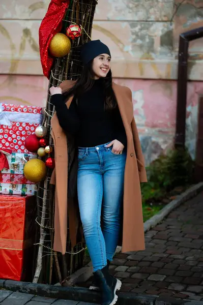 Tatil sezonu için ışıl ışıl süslenmiş genç bir kadın, canlı renkler ve süslemelerle dolu şenlikli bir gösteriye yaslanarak neşe ve stil dolu bir anın tadını çıkarıyor..