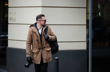 İyi giyimli bir adam, serin ve bulutlu bir günde şehir hayatının özünü yakalamak için elinde kamerayla sokakta güven içinde yürür..