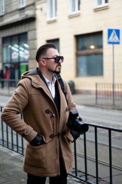 Şen şehirli bir ortamda, şık bir adam, elinde bir kamerayla, parlak bir öğleden sonra sokağın canlı atmosferinin keyfini çıkarırken kendine güvenerek ayakta duruyor..