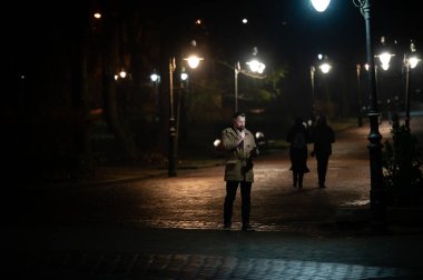 Gece gezginleri, parlayan sokak lambalarıyla aydınlatılan kaldırım taşından bir patika boyunca dolaşır, gece gezintileri için samimi, davetkar bir atmosfer yaratır..
