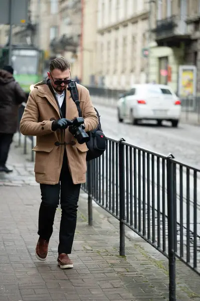 Sıcak palto ve gözlüklü bir adam hareketli bir caddede yürüyor, fotoğraf makinesiyle anlık anları yakalıyor ve canlı atmosferde sırılsıklam oluyor..