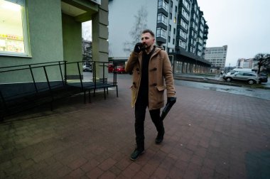 Şık bir palto giymiş odaklanmış bir birey şehir kaldırımında yürüyor, bir telefon görüşmesi yapıyor, alacakaranlık çökerken kentsel yaşamın enerjik özünü somutlaştırıyor..