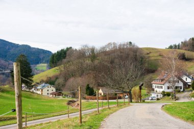Yuvarlanan tepeler sakin bir zemin oluşturur. Dolambaçlı bir yol, yemyeşil yemyeşil evlerle çevrili, bulutlu bir günde huzurlu bir kırsal alan oluşturur..