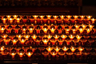 Mumlar kutsal bir yerde hafifçe titreşiyor, karanlığa hafif bir ışık tutuyor. İnsanlar şehrin akşam aktiviteleri arasında durup düşünmek, dua etmek ve teselli aramak için duruyorlar..