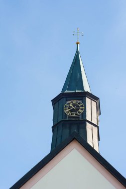 Sarp yeşil çatılı ve karmaşık saat yüzlü çarpıcı bir saat kulesi sabah saatlerinde köyün huzurlu cazibesini yansıtan masmavi gökyüzüne karşı dimdik ayakta duruyor..