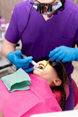 Genç bir hasta dişçi koltuğunda oturur ve iyi aydınlatılmış bir klinik ortamında gerekli aletleri ve hijyen uygulamalarını kullanarak düzenli bir sağlık kontrolü yapar..