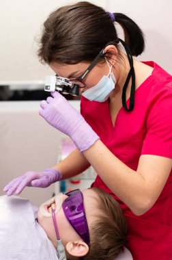 Kendini işine adamış bir dişçi renkli bir diş kliniğinde genç bir hastaya yardım eder, önemli bir ağız kontrolü sırasında detaylara çok dikkat ederek konfor ve güvenliği sağlar..