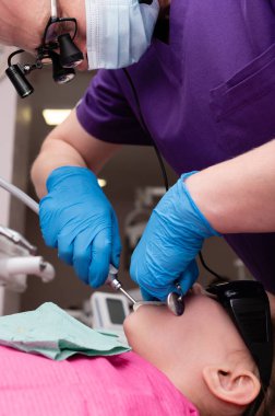 Parlak ışıklandırılmış diş sağlığı kliniğinde eldiven ve maske takan yetenekli bir dişçi, rahat ve güvenli bir şekilde diş tedavisi gören bir çocuğa nazikçe bakıyor..