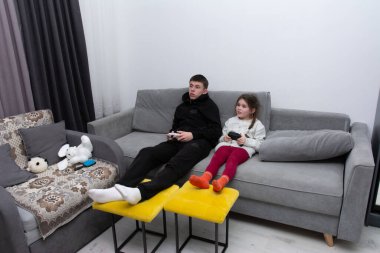 İki kardeş şık bir kanepede rahatça oturuyorlar, heyecan verici bir oyun seansına dalmışlar. Şakacı arkadaşlıkları oturma odasının atmosferini aydınlatıyor..