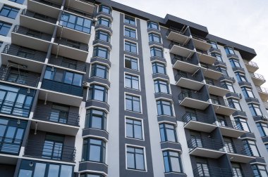 Çağdaş bir apartman kompleksi berrak bir gökyüzüne karşı dimdik ayakta duruyor. Gösterişli balkonları ve çevresindeki canlı şehir yaşamını yansıtan büyük pencereleri var..