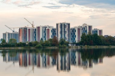 Yeni inşa edilmiş kentsel binalar sakin bir göl kıyısında dimdik duruyorlar. Yansımaları, sabah güneşinin ışıldamaya başladığı güzel bir manzara yaratıyor..
