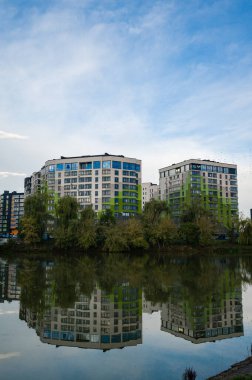 Gösterişli apartman yapıları dingin suların üzerinde yükselir, canlı renkleri mükemmel bir şekilde yansıtılır, açık bir günde rahatlatıcı bir atmosfer yaratır..
